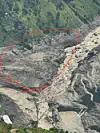 Red outline marking a former village site amid rocky landslide debris on a steep mountain slope.