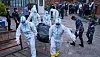 People in white protective suits carry a covered body through a crowd in Kathmandu.