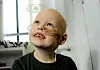 Smiling child with a shaved head and a tube in their nose in a hospital room.