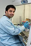 Researcher in protective clothing and gloves handles laboratory samples inside a safety cabinet.