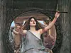 Painting of a woman in a grey dress raising her arms inside a circular wooden opening.