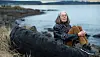 Anne Carson sits on a large tire by the sea in Reykjavík.